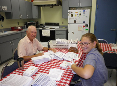 2 volunteers stuffing newsletters into envelopes.